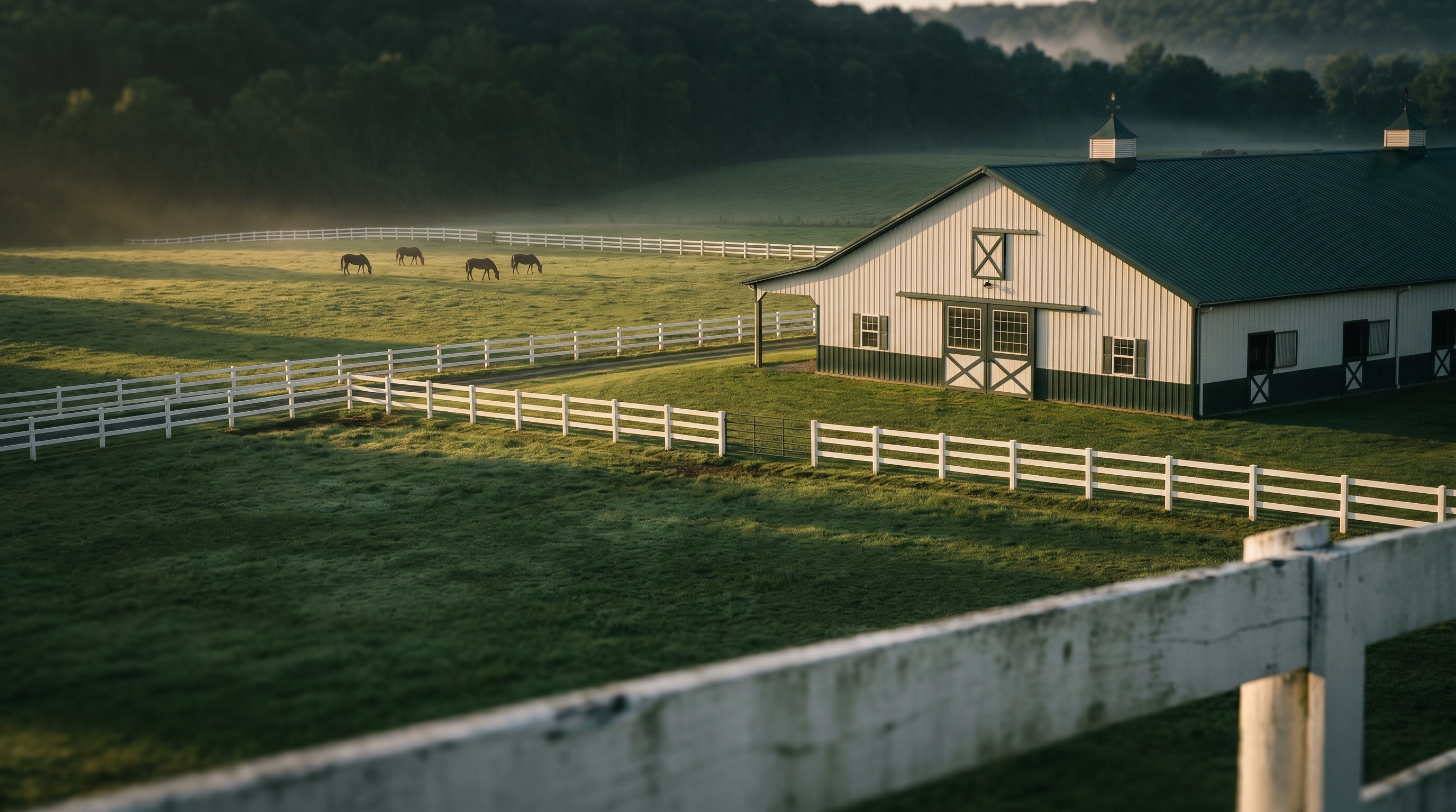 Aerial view of a white barn, fenced paddocks, and grazing horses on rolling hills, illustrating horse boarding in Warren County NJ
